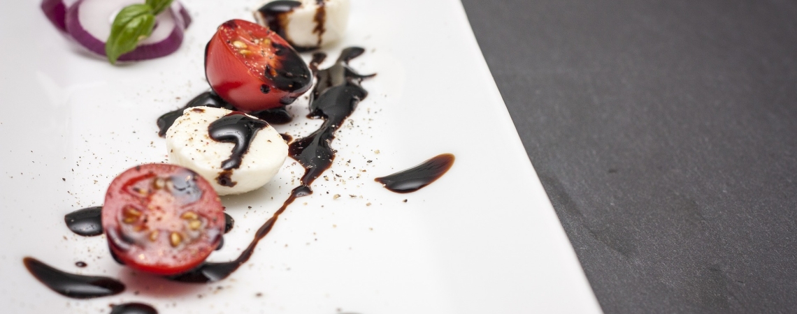 Mozzarella und Tomaten auf Teller mit Balsamico-Soße und Basilikum garniert.