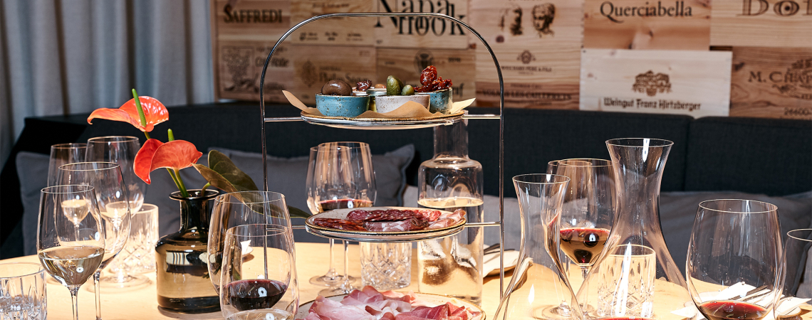 Edler gedeckter Tisch mit Wein und Etagere voller Delikatessen, dekoriert mit roten Blumen.