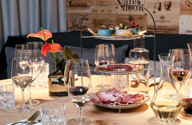 Edler gedeckter Tisch mit Wein und Etagere voller Delikatessen, dekoriert mit roten Blumen.