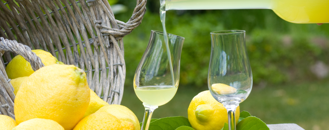 Ein gefülltes Glas Limoncello neben einem Korb voller Zitronen.