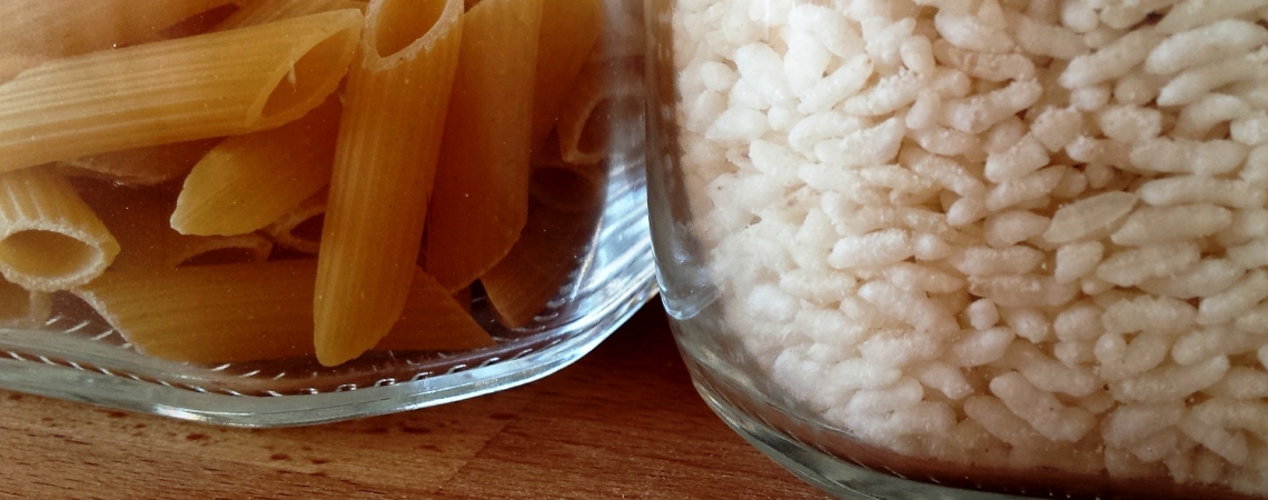 Zwei Glasbehälter mit Penne und Reis auf Holzoberfläche.