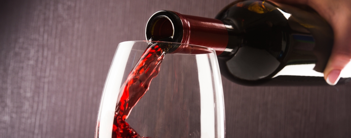 Rotwein wird in ein Glas auf dunklem Hintergrund gegossen.