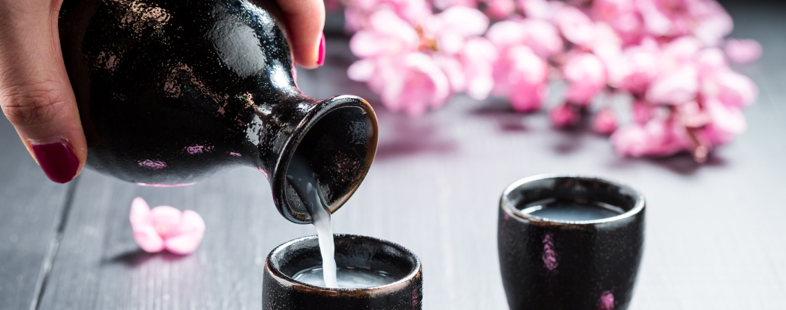 Schwarze Karaffe und Tassen mit blühenden Kirschblüten im Hintergrund.