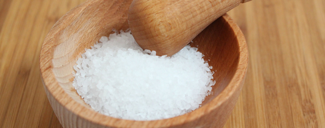 Holzschale mit grobem Salz und Holzstößel auf Holzuntergrund.