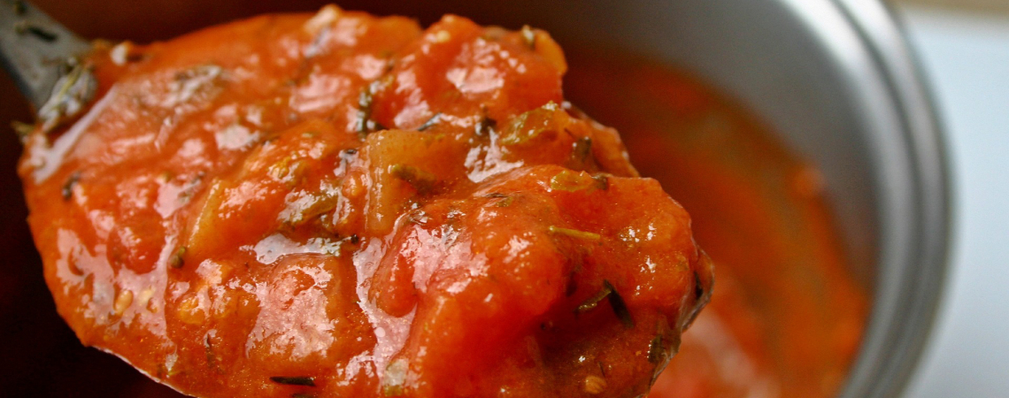 Rote Tomatensoße mit Kräutern auf einem Löffel.