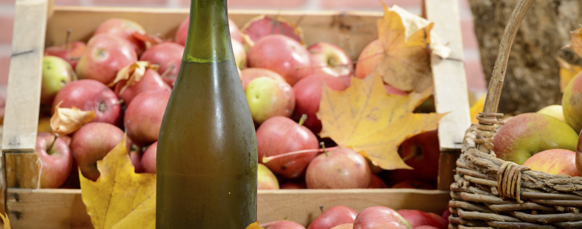Grüne Flasche vor Kiste mit roten Äpfeln und Herbstblättern.