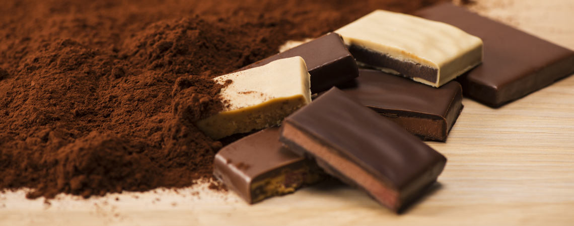 Verschiedene Schokoladentafeln und Kakaopulver auf hellbraunem Untergrund.