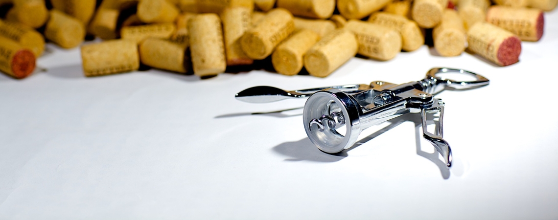 Silberner Korkenzieher vor einem Haufen Weinkorken auf weißem Hintergrund.