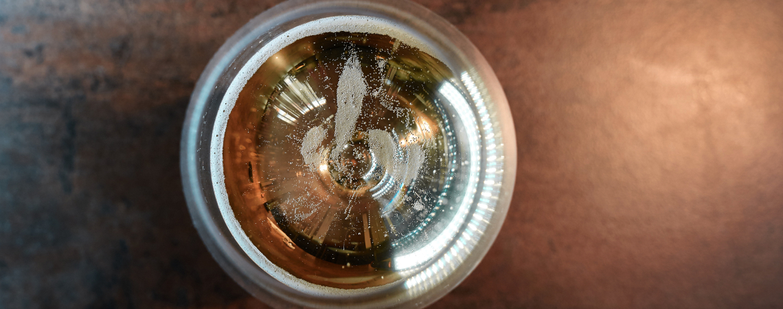 Glas Bier von oben mit Schaum und Kohlensäure auf dunklem Tisch.