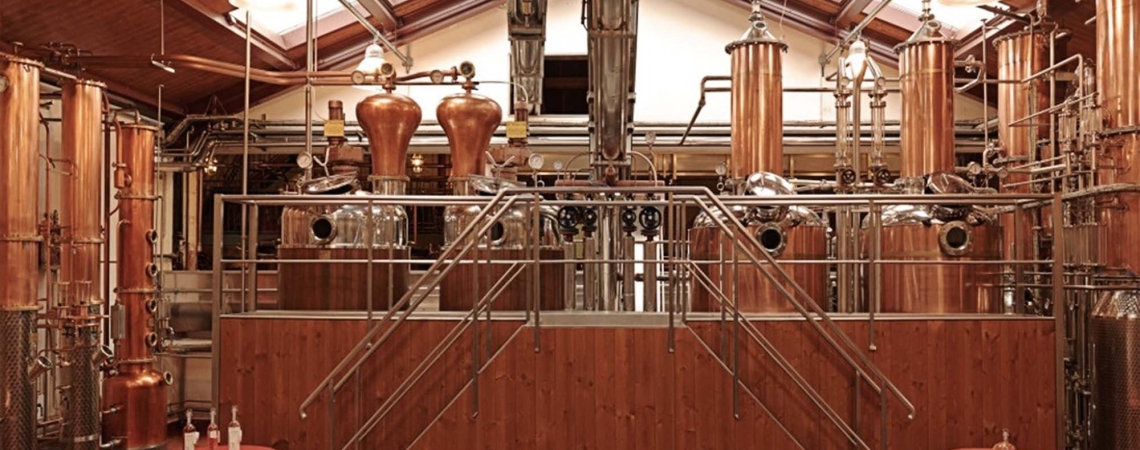 Kupferne Destillationsanlage mit glänzenden Rohren und Tanks in einem holzverkleideten Raum.