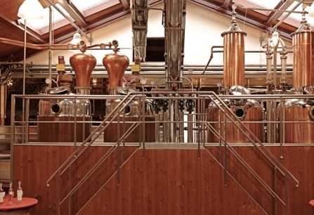 Kupferne Destillationsanlage mit glänzenden Rohren und Tanks in einem holzverkleideten Raum.