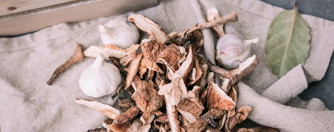 Getrocknete Pilze und Knoblauch auf Leinentuch, dekoriert mit Lorbeerblättern.
