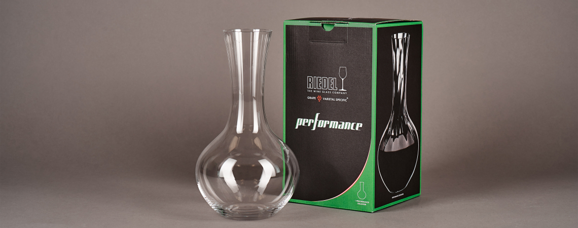 Glasdekanter vor einer schwarzen, grünen Verpackung auf grauem Hintergrund.