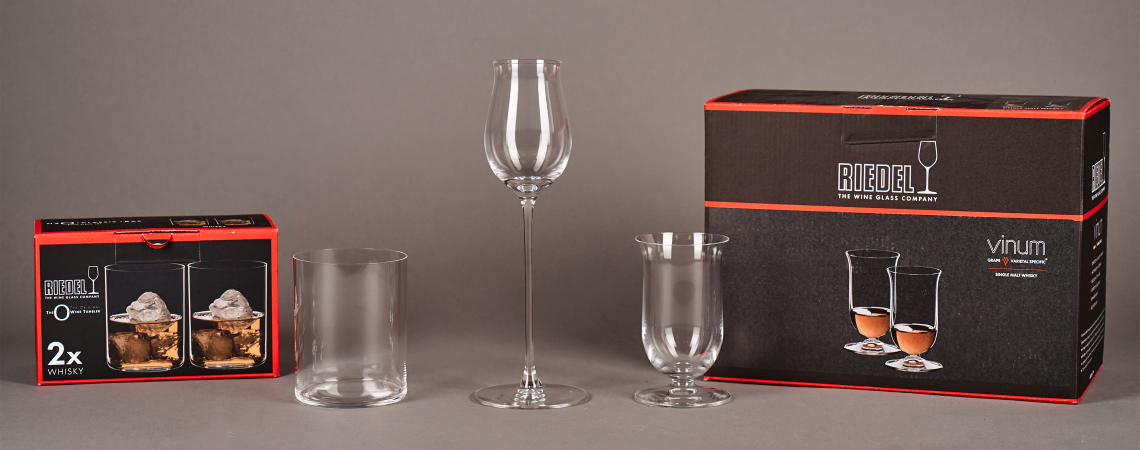 Vier Riedel-Gläser verschiedener Formen vor zwei schwarzen Verpackungen.