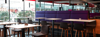 Moderne Café-Innenansicht mit lila Polstersitzbank und Holztischen, umgeben von Stühlen.