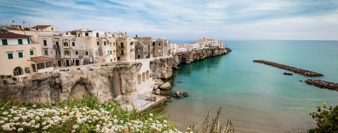Küstenstadt mit pastellfarbenen Gebäuden auf Klippen, umgeben von türkisblauem Meer.