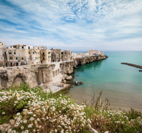 Küstenstadt mit pastellfarbenen Gebäuden auf Klippen, umgeben von türkisblauem Meer.