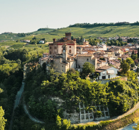 Mittelalterliche Burg auf einem grünen Hügel, umgeben von einem malerischen Dorf und Weinbergen.