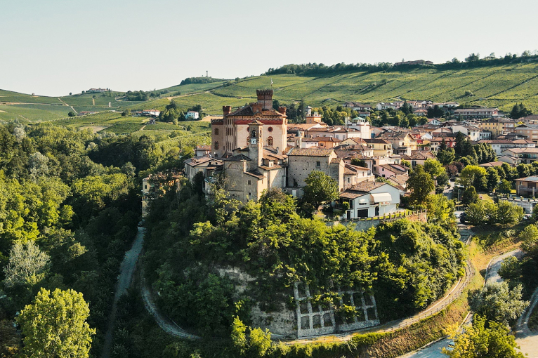Mittelalterliche Burg auf einem grünen Hügel, umgeben von einem malerischen Dorf und Weinbergen.