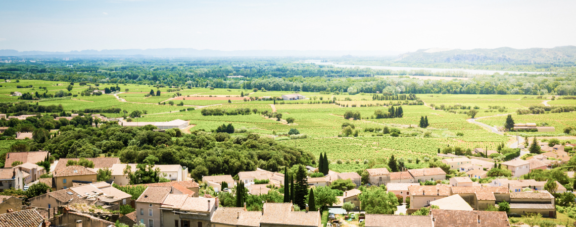 Mittelmeer-Dorf mit roten Ziegeldächern, umgeben von grünen Feldern und Landschaft.