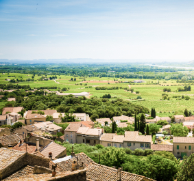 Mittelmeer-Dorf mit roten Ziegeldächern, umgeben von grünen Feldern und Landschaft.