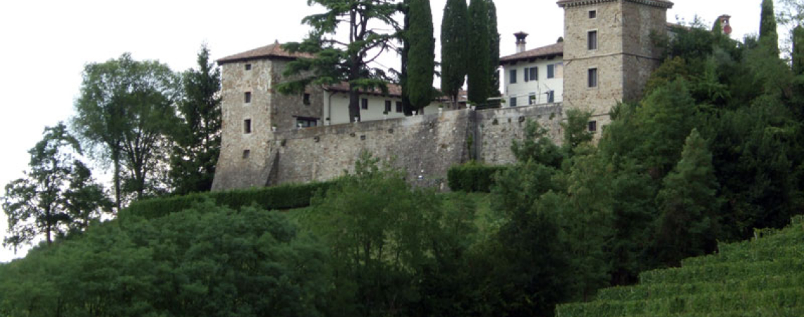 Steinburg auf Hügel, umgeben von Bäumen und Weinreben, mit Zypressen im Hof.