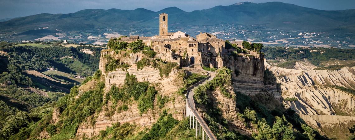 Mittelalterliches Dorf auf einem Hügel, umgeben von üppiger Landschaft und Bergkulisse.