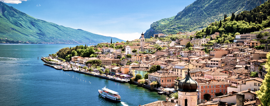 Malerische Küstenstadt mit Boot, Bergen und blauem See unter klarem Himmel.
