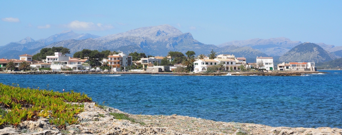 Küstenlandschaft mit Häusern, blauem Meer und entfernten Bergen unter klarem Himmel.