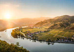 Sonnenuntergang über sanfter Flusslandschaft mit grünen Hügeln und kleinen Dörfern.