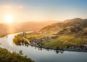 Sonnenuntergang über sanfter Flusslandschaft mit grünen Hügeln und kleinen Dörfern.