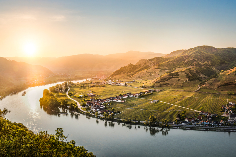 Sonnenuntergang über sanfter Flusslandschaft mit grünen Hügeln und kleinen Dörfern.