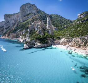 Klares türkisblaues Meer an felsiger Küste mit grünen Hügeln im Hintergrund.