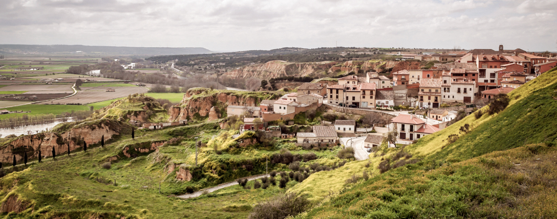 Malerische Stadt auf grünem Hügel, umgeben von weiten Feldern und leicht bewölktem Himmel.