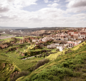 Malerische Stadt auf grünem Hügel, umgeben von weiten Feldern und leicht bewölktem Himmel.