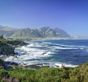 Küstenlandschaft mit blauem Meer, Bergen und grüner Vegetation unter klarem Himmel.