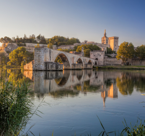 Mittelalterliche Steinbrücke über ruhigen Fluss, umgeben von historischen Gebäuden und Bäumen.