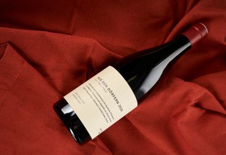 Weinflasche auf rotem Tuch mit schlichtem Etikett und rotem Verschluss.