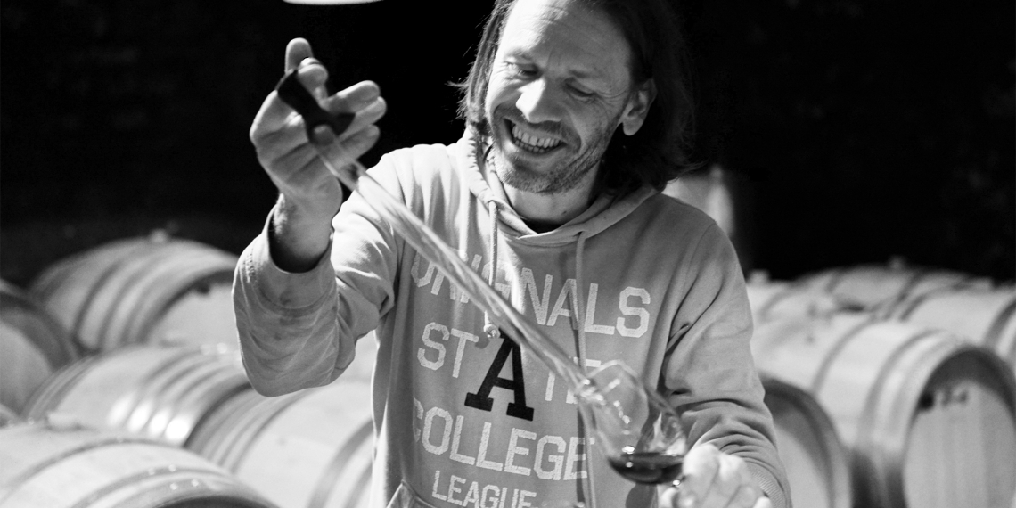 Mann in einem Weinkeller zieht Probe aus Fass.