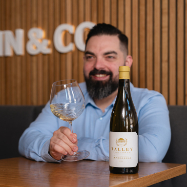 Mann mit Weinglas, Chardonnay-Flasche im Vordergrund, hölzerner Hintergrund.