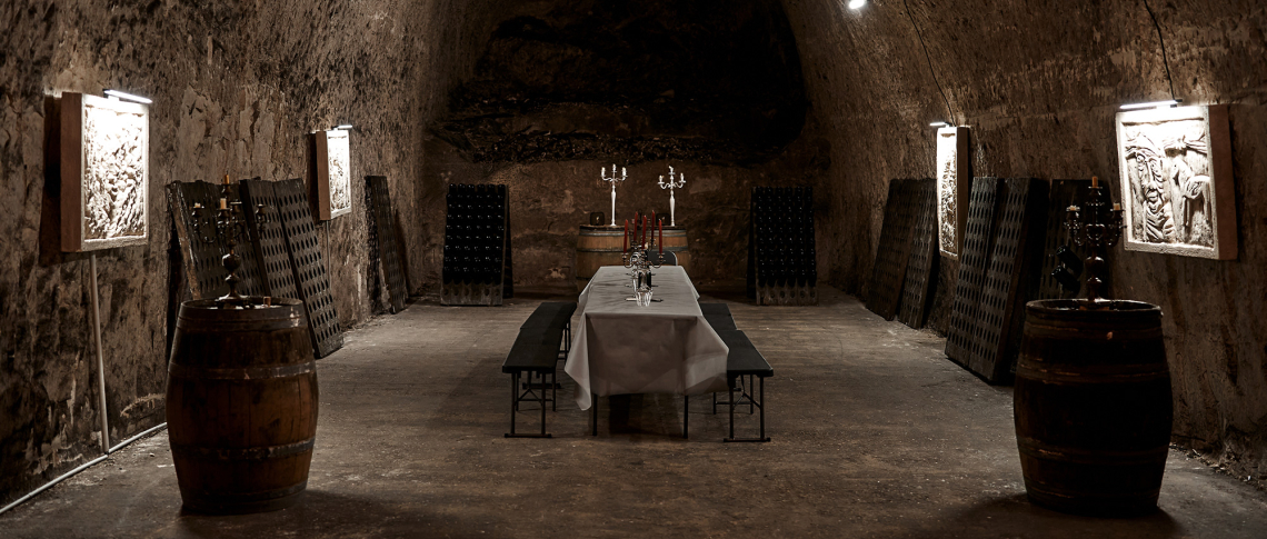 Rustikaler Weinkeller mit gedecktem Tisch, Holzfässern und schummriger Beleuchtung.