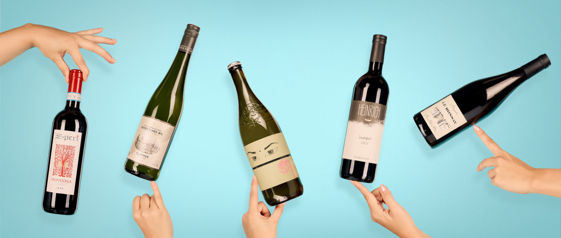 Verschiedene Weinflaschen vor blauem Hintergrund, von Händen präsentiert.