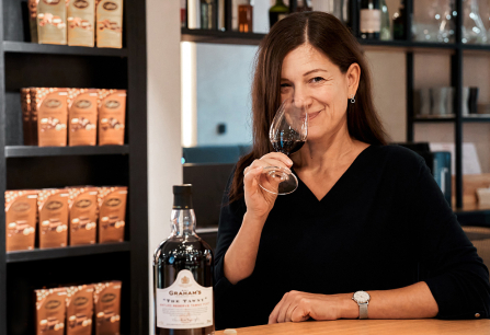 Frau riecht an einem Weinglas neben einer Getränkeflasche in einem Geschäft.