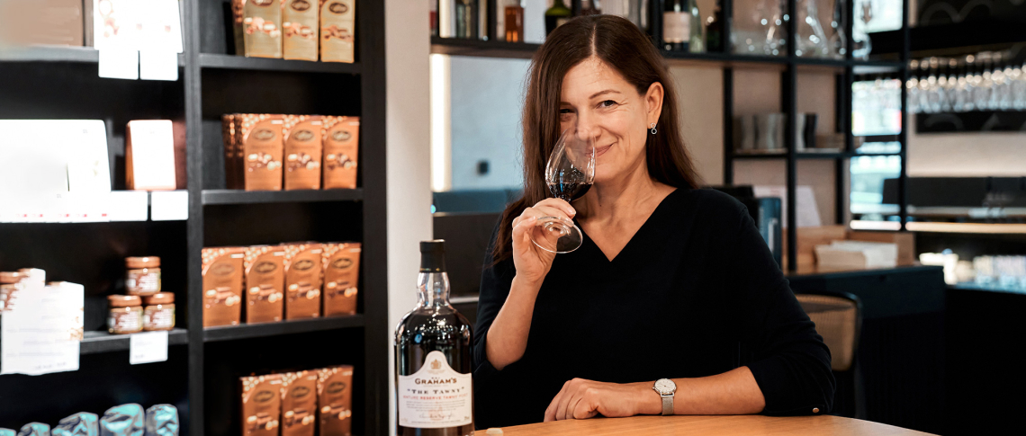 Frau riecht an einem Weinglas neben einer Getränkeflasche in einem Geschäft.