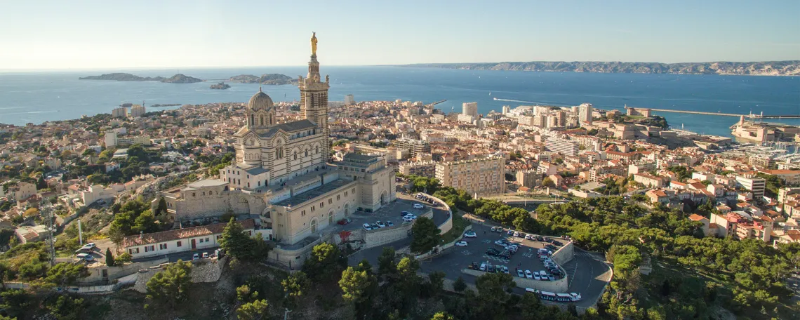 Luftaufnahme von Marseille mit Kirche, Stadt und Meer im Hintergrund.