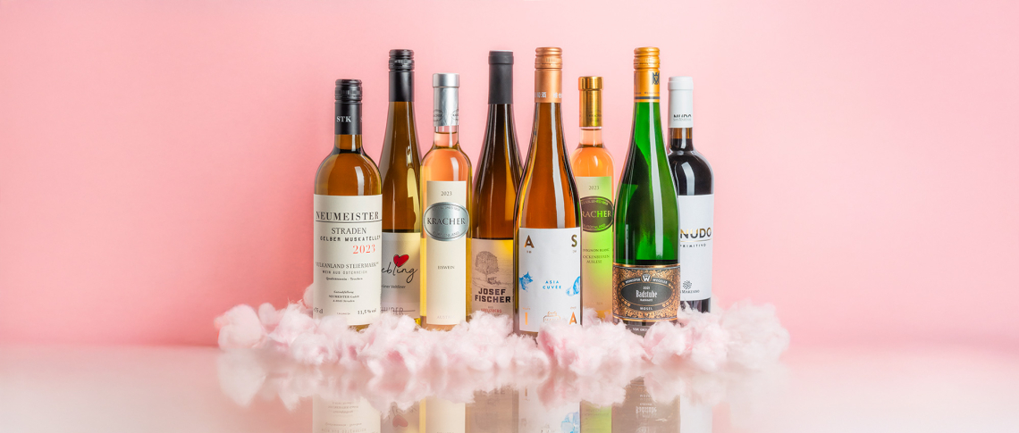 Sieben Weinflaschen auf rosafarbenem Hintergrund, umgeben von Wattewolken.