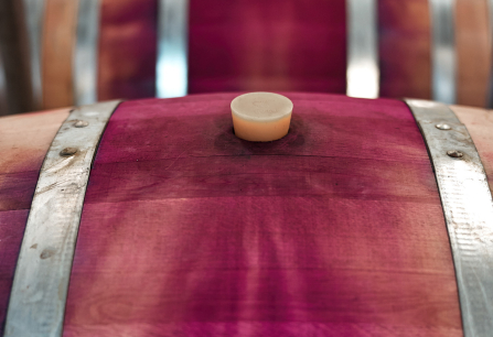 Nahaufnahme eines hölzernen Weinfasses mit purpurfarbenen Verfärbungen und Metallringen.