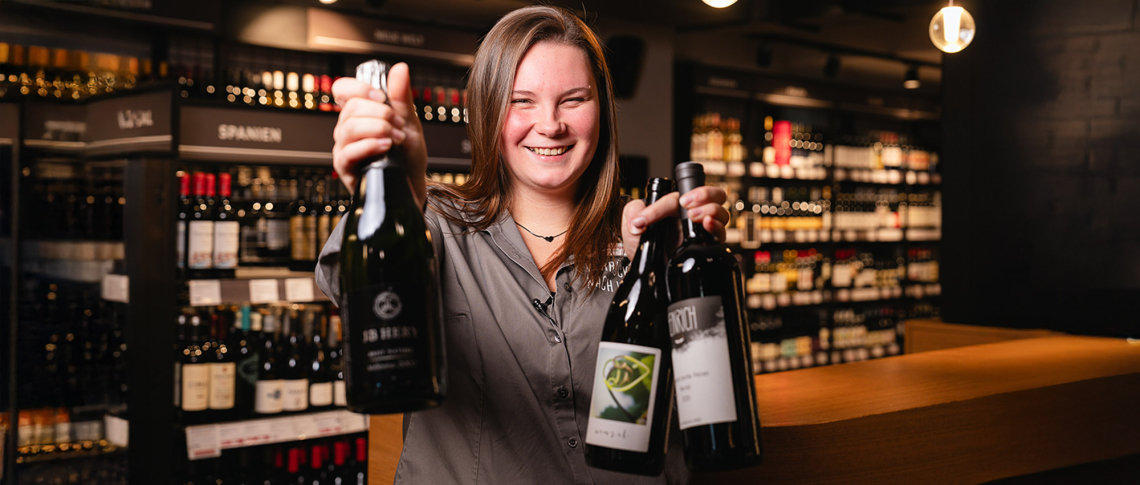 Frau hält Weinflaschen in einer stilvollen Weinhandlung.