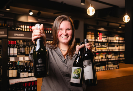 Frau hält drei Weinflaschen in einem stilvollen Weingeschäft.