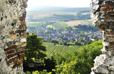 Blick durch Burgruine auf malerisches Dorf und Weinberge im Tal.
